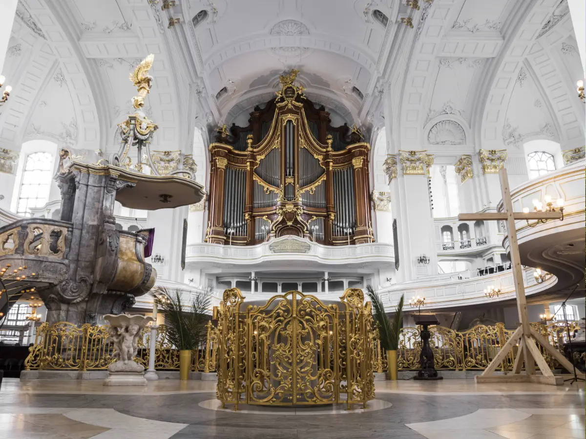 Interior of St. Michael's Church in Hamburg, Germany, featuring an ornate pipe organ, intricate gold detailing, and a high, arched ceiling.