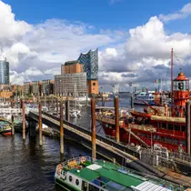 Colorful boats docked in Hamburg’s harbor with the Elbphilharmonie concert hall and modern buildings in the background.