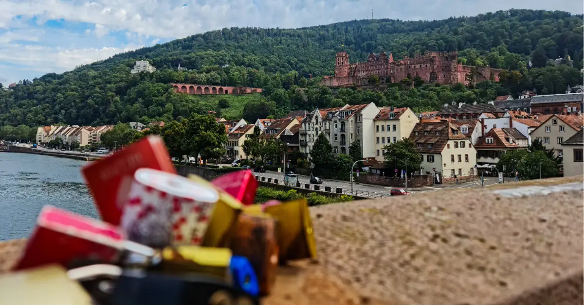 View of Heidelberg Castle on a green hillside with rows of old town houses and colorful love locks in the foreground.