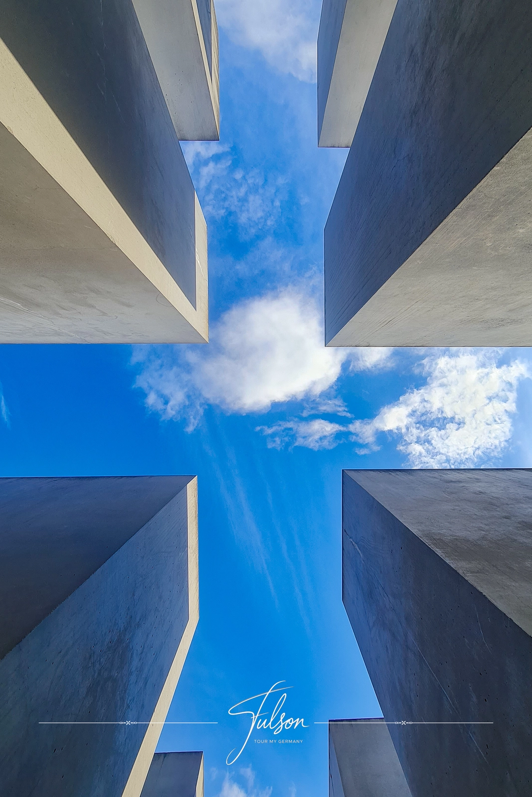 Looking up at a symmetrical architectural structure with detailed panels, flanked by walls, against a partly cloudy sky.