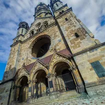 Upward angle of the war-damaged Kaiser Wilhelm Memorial Church in Berlin with Romanesque architecture and a blue sky