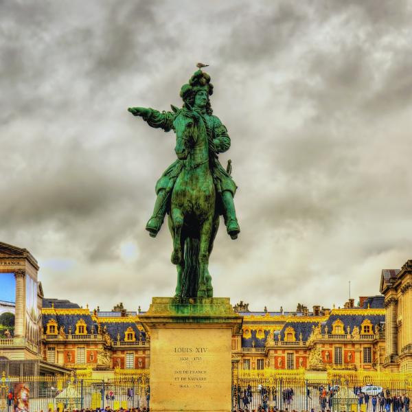 King Louis XIV statue at the Palace of Versailles in France Statue of King Louis XIV on horseback with the Palace of Versailles in the background under a cloudy sky.