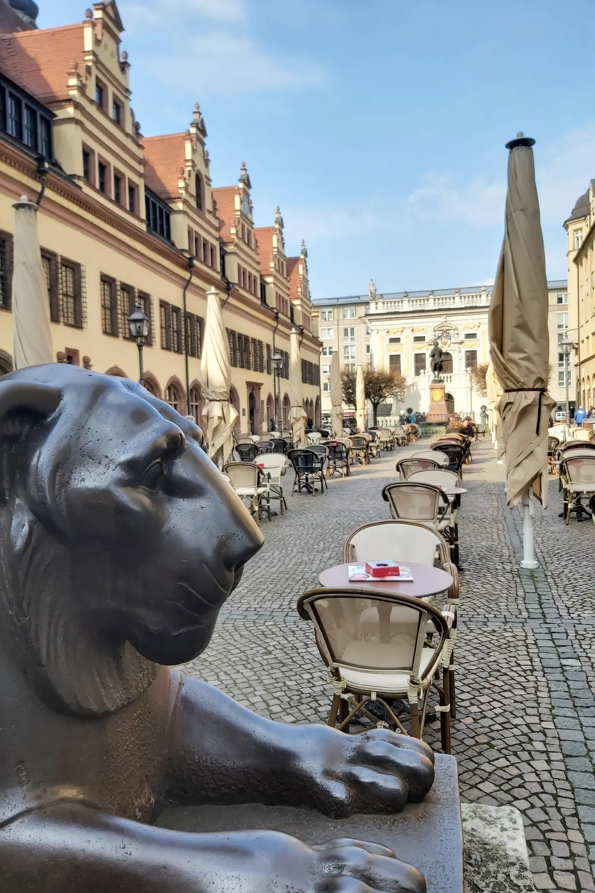 Statue of a lion in front of tables and chairs in Leipzig city centre