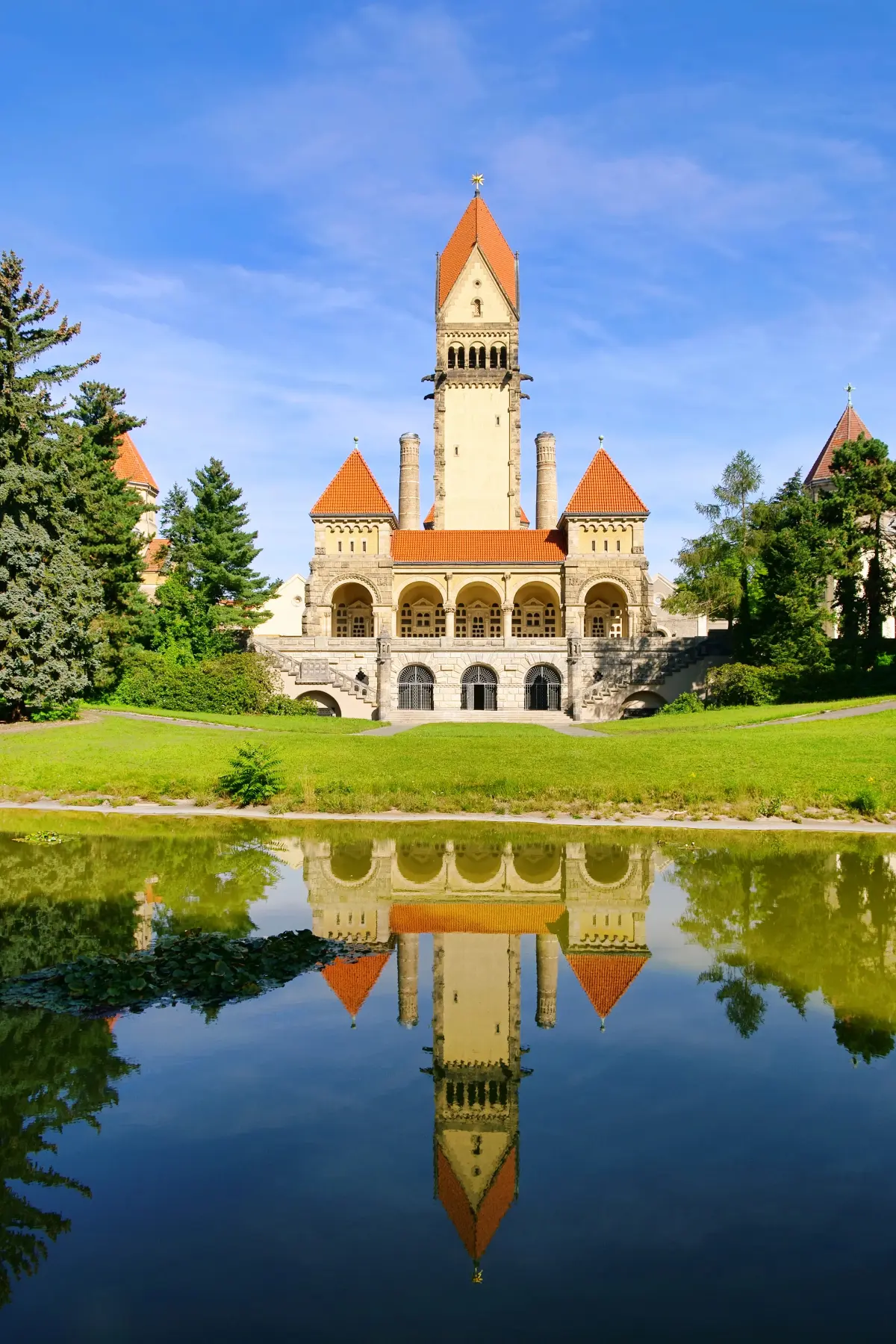 White and red chapel behind pond and trees of South Cemetery in Leipzig.