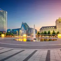 Augustusplatz in Leipzig at sunset featuring a modern glass building, central fountain, and historic architecture