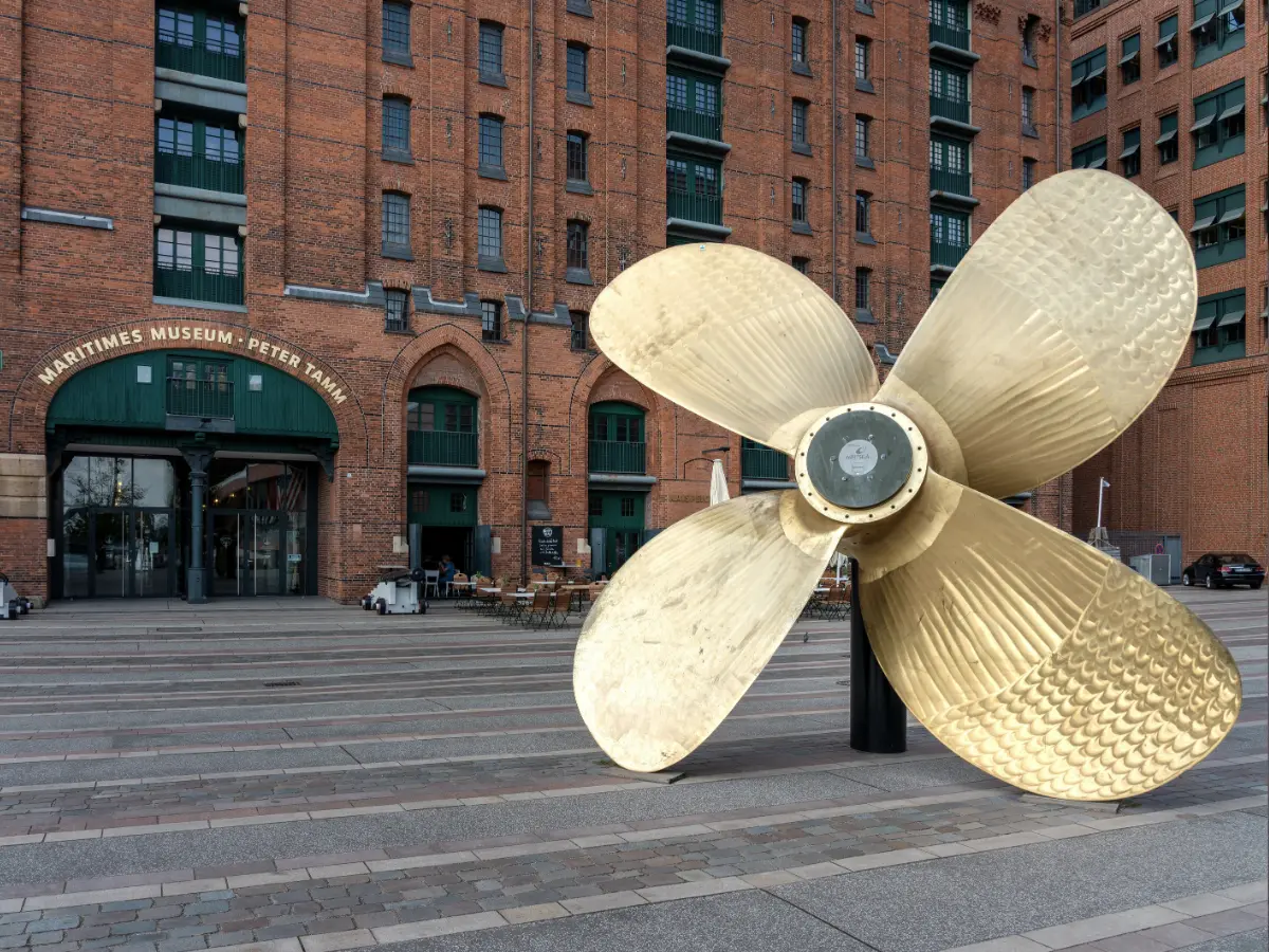 Maritime Museum in Hamburg A large brass ship propeller is displayed in front of the entrance to the Maritime Museum in a brick building.