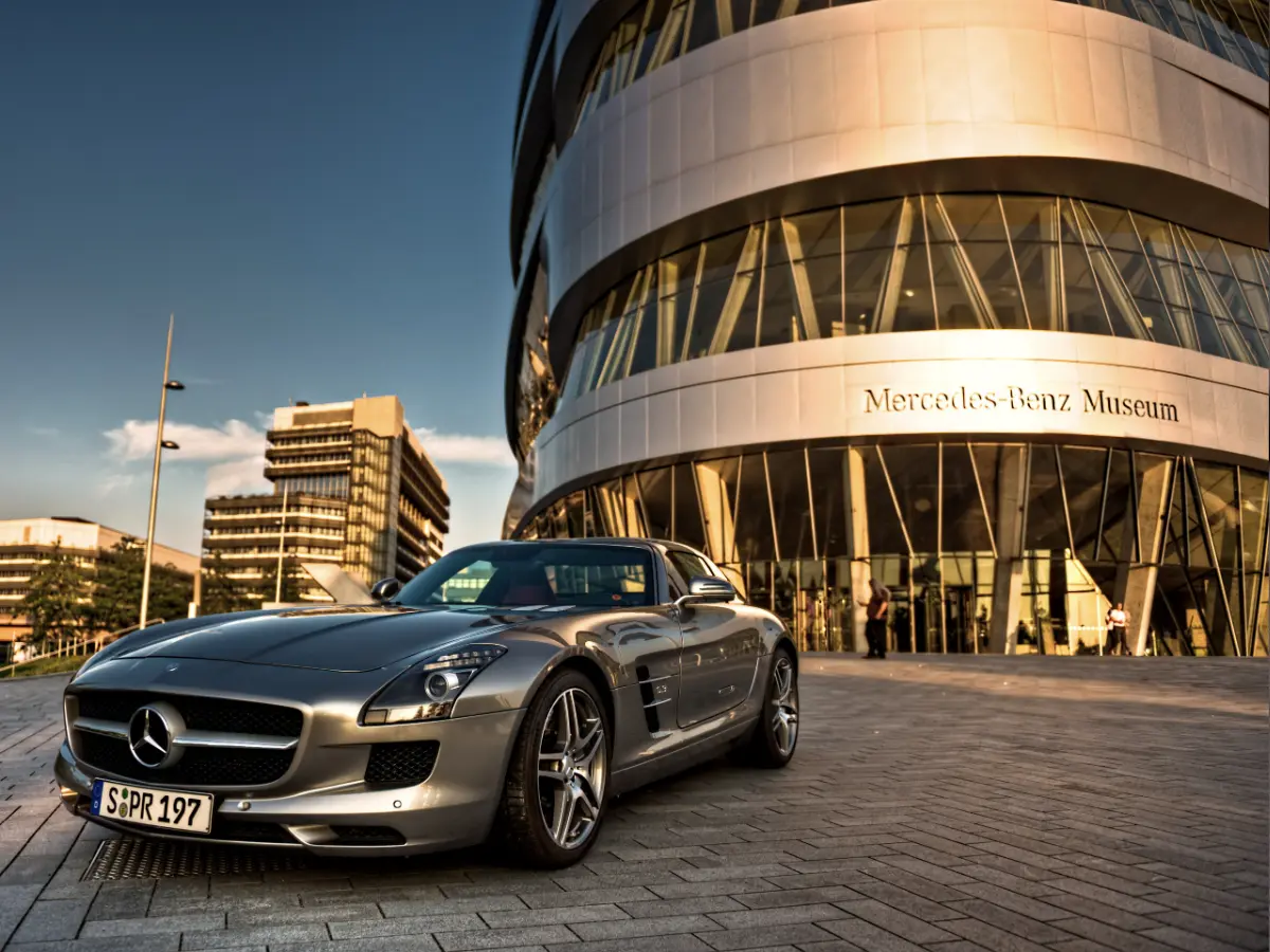 Mercedes-Benz Museum in Stuttgart Silver Mercedes-Benz sports car parked in front of the Mercedes-Benz Museum, with modern buildings and a clear sky in the background.