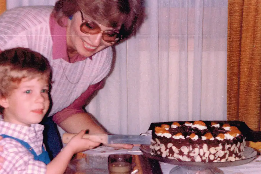 Vintage photo of a mother and young child cutting a homemade Black Forest cake together at a dining table.