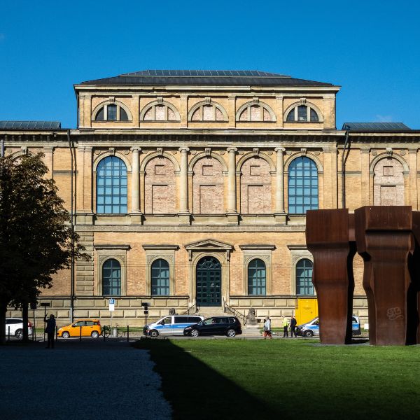 Munich Alte Pinakothek Museum as a light brown building against blue sky and rusted steel sculpture in front of it