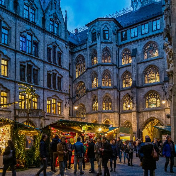 Munich Christmas Market with old Gothic buildings surrounding market stalls and people lit up by christmas lights at dusk 