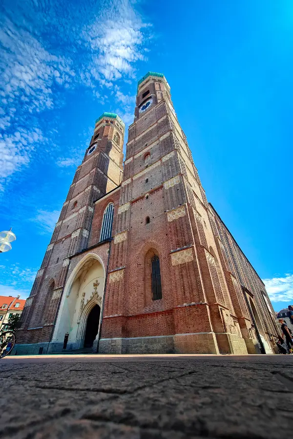Low-angle view of the tall, historic brick Frauenkirche in Munich, Germany, with two towers under a blue sky.
