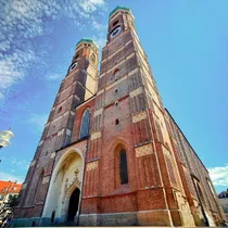 Dramatic low-angle view of Munich’s Frauenkirche twin towers with blue sky and light clouds in the background