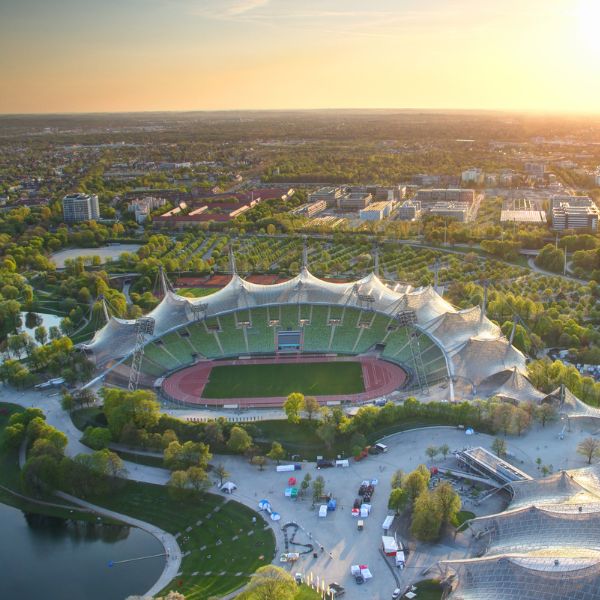 Munich Olympic Park stadium with green sports field and white tent roof and the city of munich behind it at sunset