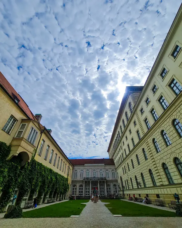 Courtyard between classical buildings with ivy-covered walls and a partly cloudy sky above.