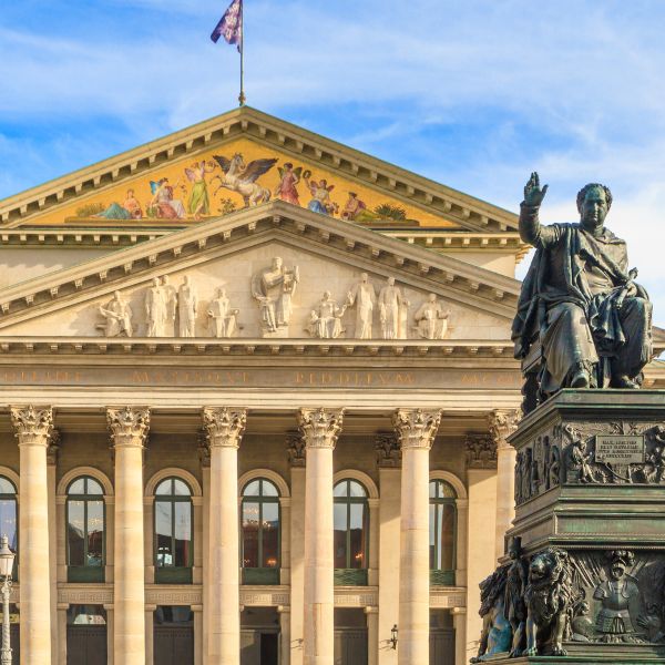 Bavarian State Opera building with light beige pillared front and statue against a lightly cloudy sky