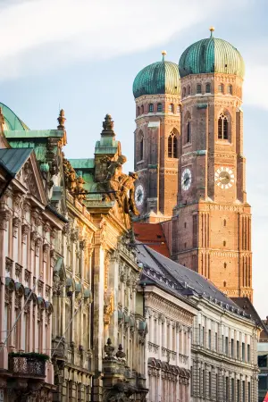 View of Frauenkirche's twin domes above historic buildings in Munich, Germany, under a clear sky.
