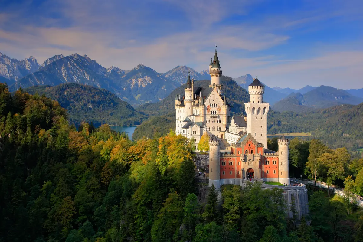 Neuschwanstein Castle set against a backdrop of mountains and forest, under a clear blue sky.