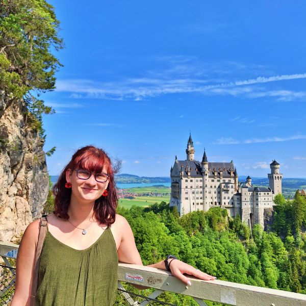 woman in front of fairy tale castle surrounded by trees
