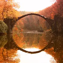 The iconic Rakotzbrücke (Devil’s Bridge) in Germany forms a perfect circle with its reflection, surrounded by autumn foliage.