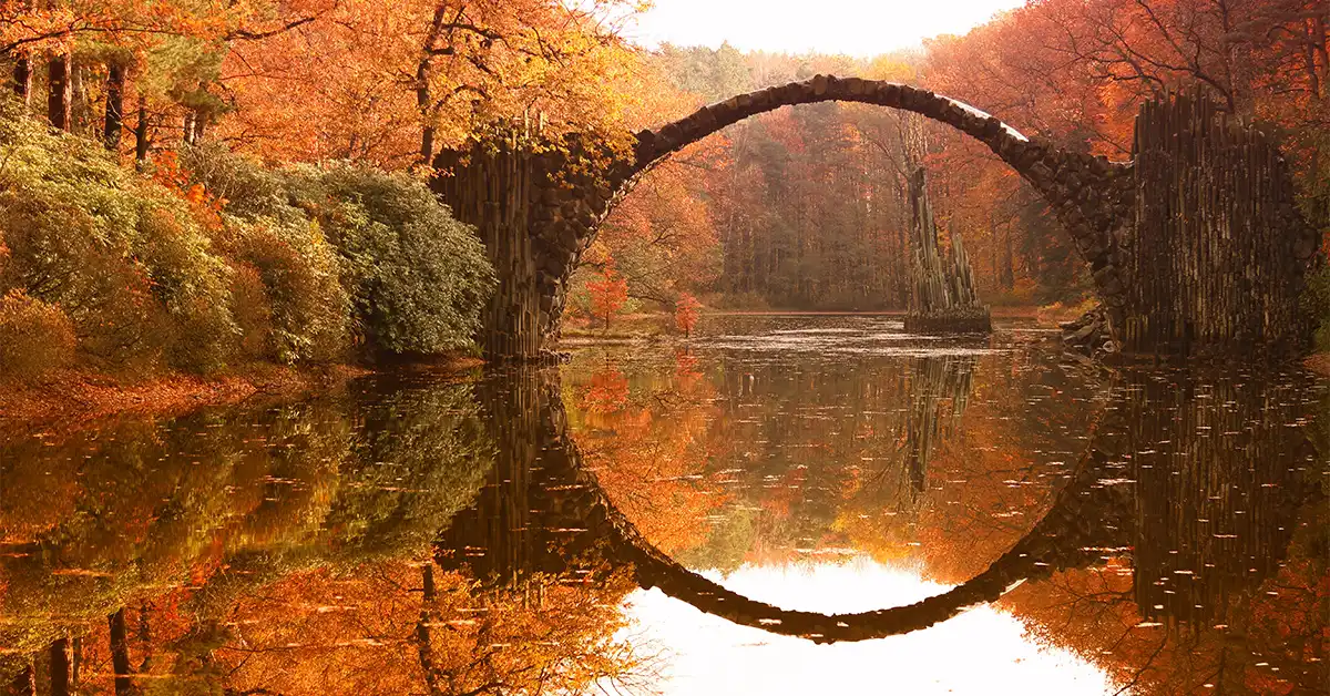 Rakotzbrücke, the Devil’s Bridge in Kromlau, Germany, reflected perfectly in the calm autumn lake surrounded by red and orange foliage. Rakotzbrücke, the Devil’s Bridge in Kromlau, Germany, reflected perfectly in the calm autumn lake surrounded by red and orange foliage.