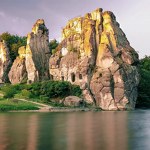 The towering Externsteine rock formations glowing in golden light, reflected in the still water below.