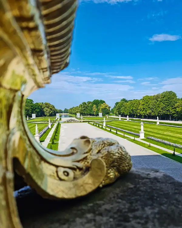 Ornate golden railing framing a view of the landscaped gardens and fountains of Nymphenburg Palace.