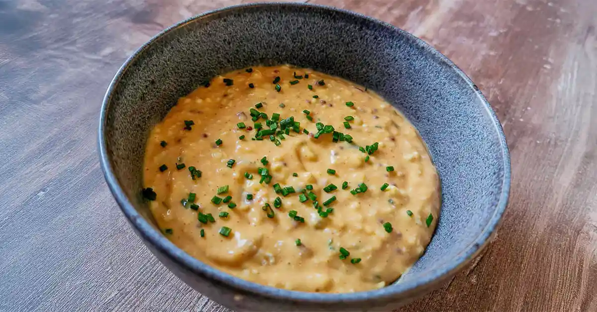 Bowl of Obatzda Bavarian beer cheese dip garnished with fresh chives, served in a rustic ceramic bowl on a wooden surface.
