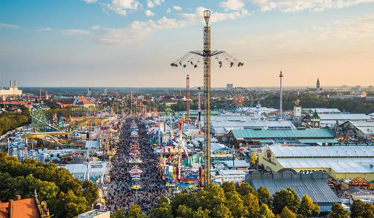 Oktoberfest festival grounds in Munich with crowds, beer tents, and carnival rides during sunset.
