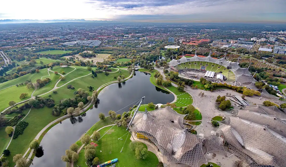 Aerial view of Munich’s Olympiapark with stadium roof and green surroundings.