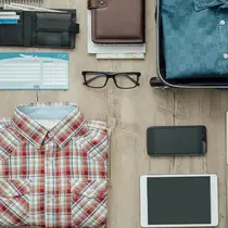Flat lay of travel essentials including clothing, tech gadgets, and accessories neatly arranged on a wooden surface