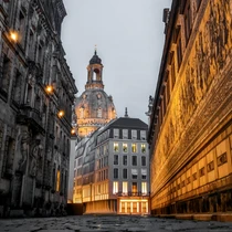 Dramatic evening view of Dresden’s Frauenkirche framed by historic buildings and the illuminated Fürstenzug mural