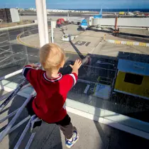 Young child watching airplanes through the glass at a German airport departure gate.