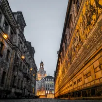 View of Dresden’s Fürstenzug mural illuminated at dusk with the Frauenkirche rising in the distance