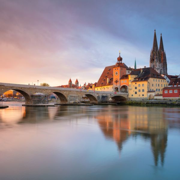 City of Regensburg, Germany buildings along water at sunset with a stone arched bridge in the City of Regensburg, Germany