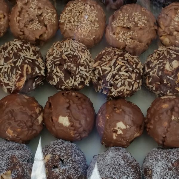 A display case with rows of assorted chocolate-covered pastries, some topped with nuts, sprinkles, and other toppings.