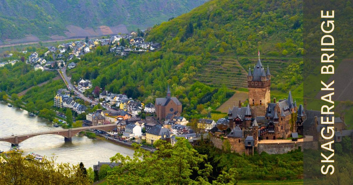 The Skagerak bridge offers a perfect photo spot. Capture the castle, valleys, and river all from one archy old bridge! A scenic view of Cochem on the Moselle River, featuring lush hills, medieval Cochem Castle, and a bridge crossing the river. Text overlay reads "SKAGERAK BRIDGE".