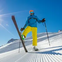 Skier in bright blue and yellow gear posing confidently on a sunlit, freshly groomed ski run.