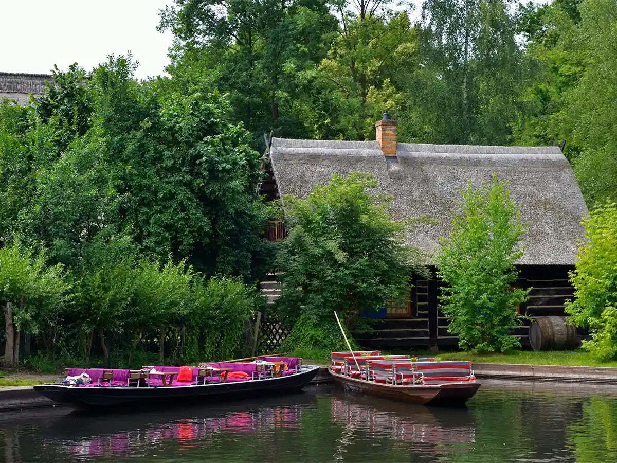 Brightly cushioned punts moored beside thatched cottage on Spreewald canal—iconic Brandenburg nature spot.
