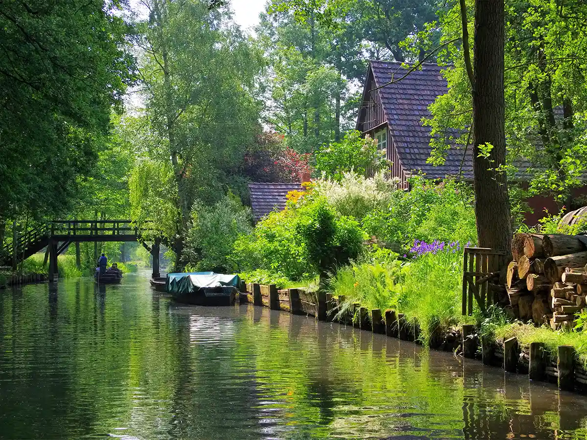 Verdant Spreewald canal with wooden house and punter under footbridge—idyllic Brandenburg itinerary highlight.