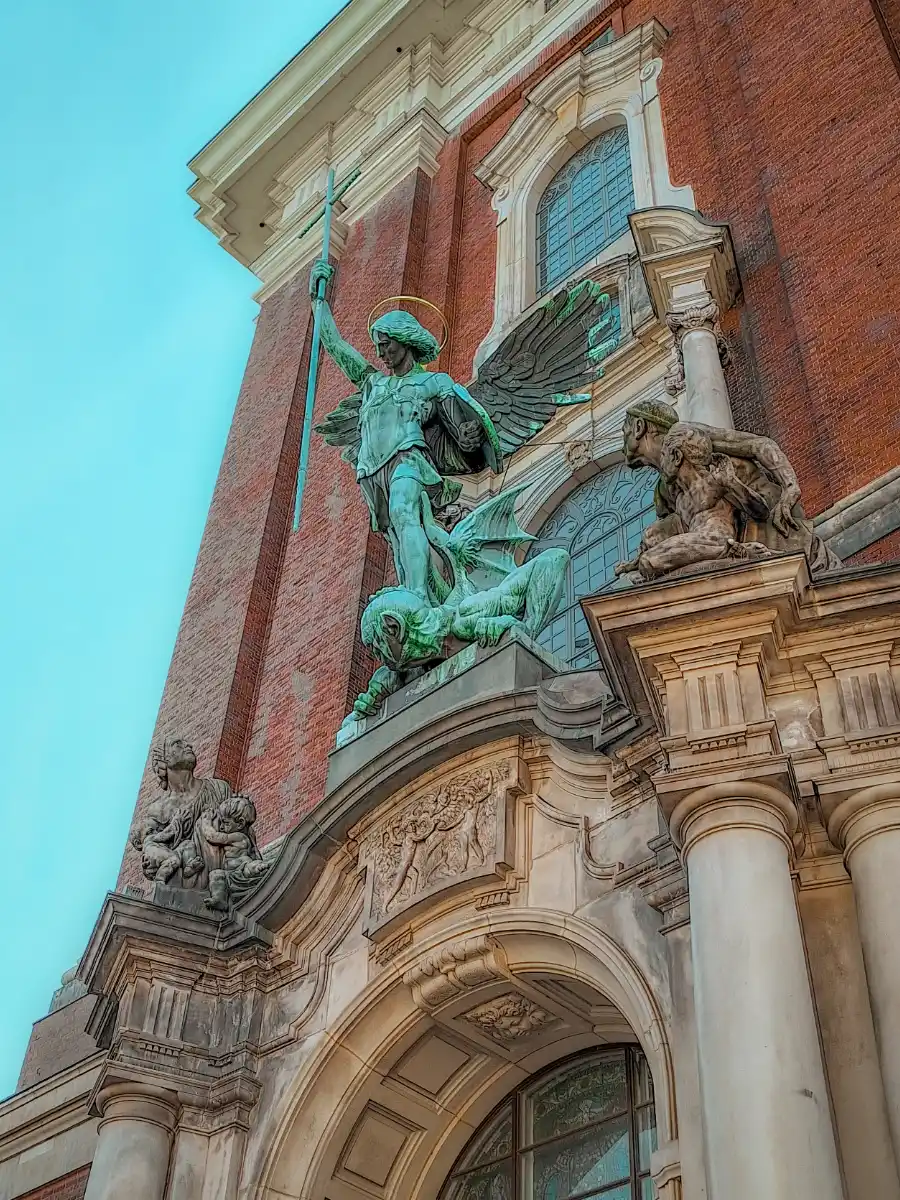 Statue of Archangel Michael defeating the devil above the entrance of St. Michael’s Church in Hamburg, with the brick façade and arched windows in view.
