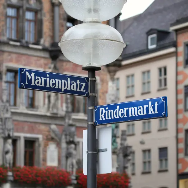 Street signs for Marienplatz and Rindermarkt on a lamp post with historic buildings in the background.