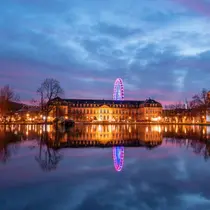 Evening view of Stuttgart’s New Palace with festive lights and a Ferris wheel reflected in a still pond