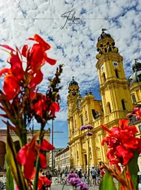 A vibrant yellow church with ornate towers stands under a partly cloudy sky, framed by red flowers. People and bicycles are visible in the plaza below.