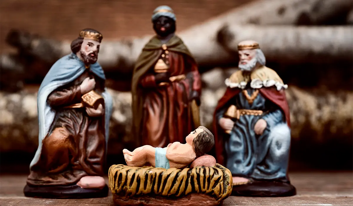 Nativity scene with three wise men figurines and baby Jesus in a manger on a wooden surface.