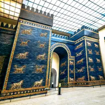 Bright blue glazed brick gate with golden animal reliefs, displayed inside a glass-roofed museum hall.