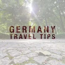 Sunlight filtering through trees above a cobblestone path with the text ‘Germany Travel Tips’ in bold lettering
