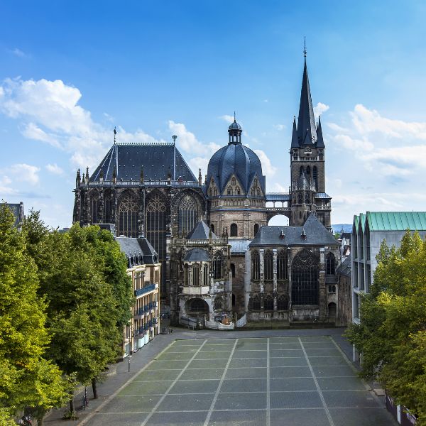 Aachen Cathedral in Aachen, Germany. A UNESCO site. A gray cathedral with spire and dome in front of tree lined square.