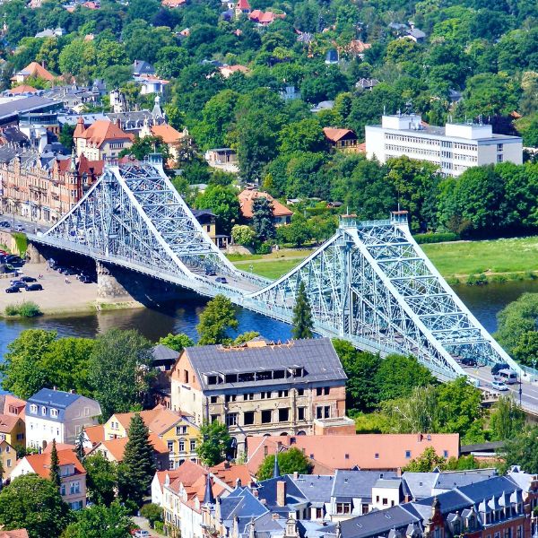 Iron bridge known as Blue Wonder Bridge spanning the Elbe River, Dresden. Various buildings and trees surround the bridge