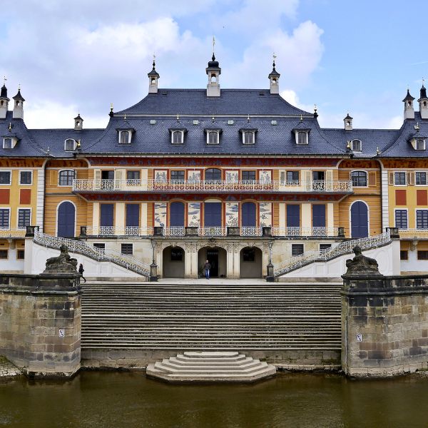 Grey roof and orange facade of Pillnitz Palace with steps leading down to the Elbe River in Dresden