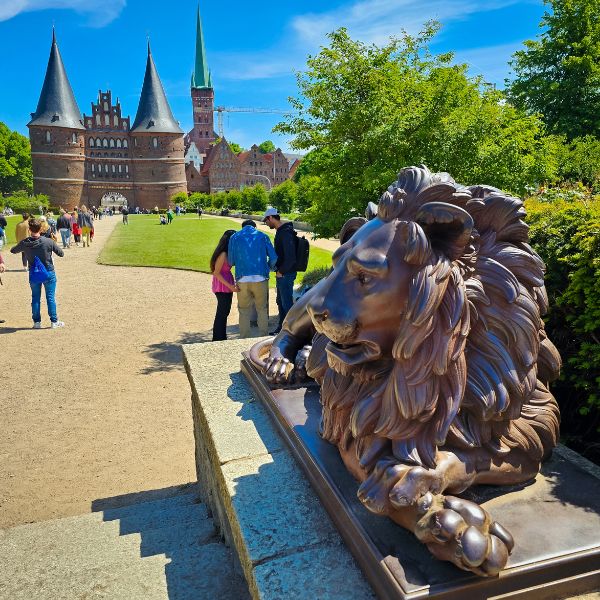 statue of lion in front of twin spired red brick gate and church tower, in Lübeck, Germany